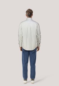 Wit button-down shirt met verticale grijze strepen, relaxed fit, lange mouwen, gecombineerd met blauwe denim broek en witte sneakers.