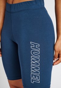 Marineblauwe sportshorts van zachte, rekbare stof. Voorzien van een brede elastische tailleband en een verticale witte logo aan de zijkant.