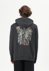 Sudadera negra de material suave, con un dise�ño gráfico de dos lobos feroces y un personaje, con acentos coloridos en la parte trasera.