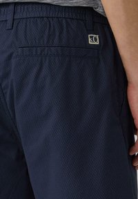 Marineblauwe shorts met een gestructureerd patroon, elastische tailleband en een enkele achterzak. Voorzien van een klein merkembleem op de tailleband.