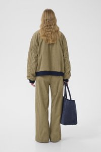 Geacă matlasată supradimensionată în carouri verzi cu accente bleumarin, asortată cu pantaloni cu croială largă în aceeași nuanță. Poartă o geantă tote din piele intoarsă albastru închis.