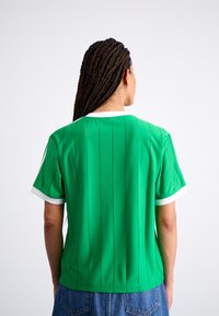 Blusa verde de manga corta con rayas verticales, ribete blanco en el cuello y las mangas, textura suave y corte relajado.