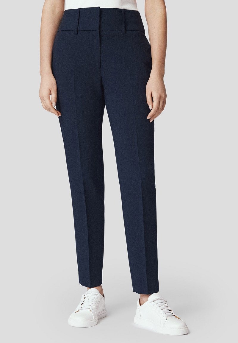 Granatowe spodnie o kroju spodni eleganckich z wysokim stanem, przeszyciami z przodu i gładką teksturą, zestawione z białymi trampkami. Prosty i nowoczesny design.