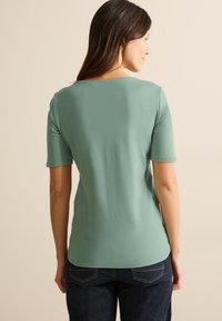 Tričko s krátkým rukávem v mátově zelené barvě vyrobené z jemné látky. Má kulatý výstřih a pohodlný střih. Kombinováno s tmavými džínami.