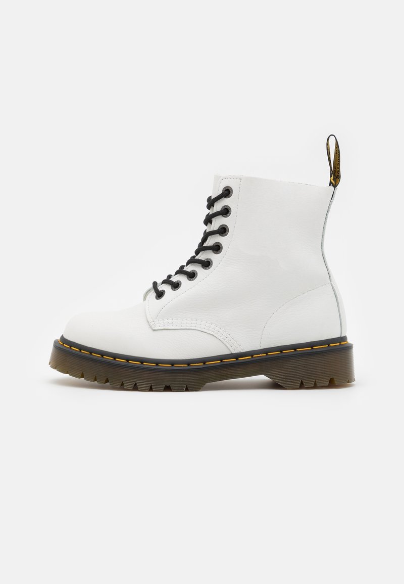 Botte de combat blanche en cuir avec des lacets noirs, une couture jaune sur la semelle noire, et une languette de tirage noire et jaune à l'arrière.