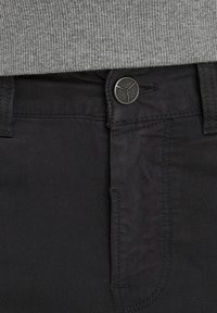 Pantalones de algodón negros con una textura suave, que cuentan con un cierre de botón y cremallera, detalles de costura sutiles y bolsillos frontales estándar.