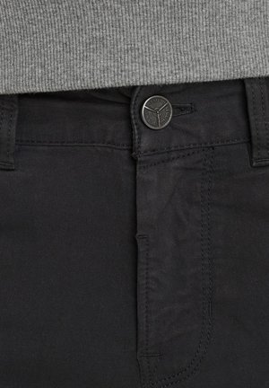 Pantalones de algodón negros con una textura suave, que cuentan con un cierre de botón y cremallera, detalles de costura sutiles y bolsillos frontales estándar.