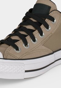 Μπεζ καμβάς sneaker με ψηλό πέλμα, μαύρα κορδόνια, ασημί οπές, λευκή λαστιχένια σόλα και μαύρη λεπτομέρεια ρίγα κοντά στην άκρη της σόλας.