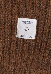 Hnědá tkanina z umělého vlákna s výraznou bílou nálepkou s textem "Marc O'Polo DENIM" a pokyny pro údržbu. Texturovaná, s vertikálním žebrov�áním.