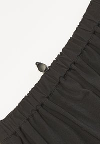 Tissu noir à texture froncée, avec une petite fermeture à bouton noir. Mise au point sur la ceinture élastique et la surface lisse.