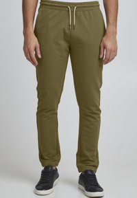 Olivgrüne Jogginghosen aus einem weichen Stoff, mit einem elastischen Taillenbund und Kordeln sowie elastischen Bündchen an den Knöcheln. Kombiniert mit schwarzen Turnschuhen.