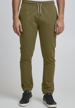 Olivgrüne Jogginghosen aus einem weichen Stoff, mit einem elastischen Taillenbund und Kordeln sowie elastischen Bündchen an den Knöcheln. Kombiniert mit schwarzen Turnschuhen.
