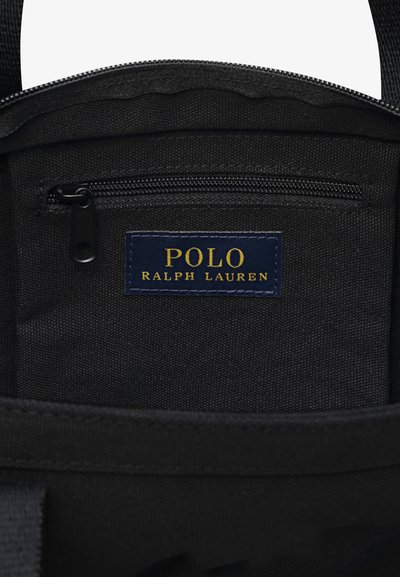 Εσωτερικό μαύρου υφασμάτινου σακιδίου με τσέπη με φερμουάρ. Μια μπλε ετικέτα με χρυσό κείμενο γράφει «POLO RALPH LAUREN». Είναι ορατές οι λεπτομέρειες στις ραφές.