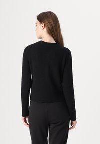 Maglione nero a maglia con maniche lunghe, scollatura tonda e orlo a costine, che presenta una texture morbida e una silhouette aderente. Design leggero e semplice.