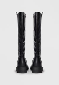 Pair of black tall leather boots with thick soles and back pull tabs, shown from the rear against a plain background.