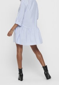 Gestreepte jurk in lichtblauw en wit, met een uitlopende onderrand en driekwartmouwen. Gecombineerd met zwarte enkelhoge laarzen met hak.