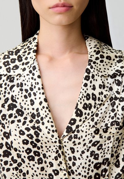 Blusa de seda con estampado de leopardo, con un escote en V profundo, manchas negras sobre un fondo crema y un bolsillo en el pecho.