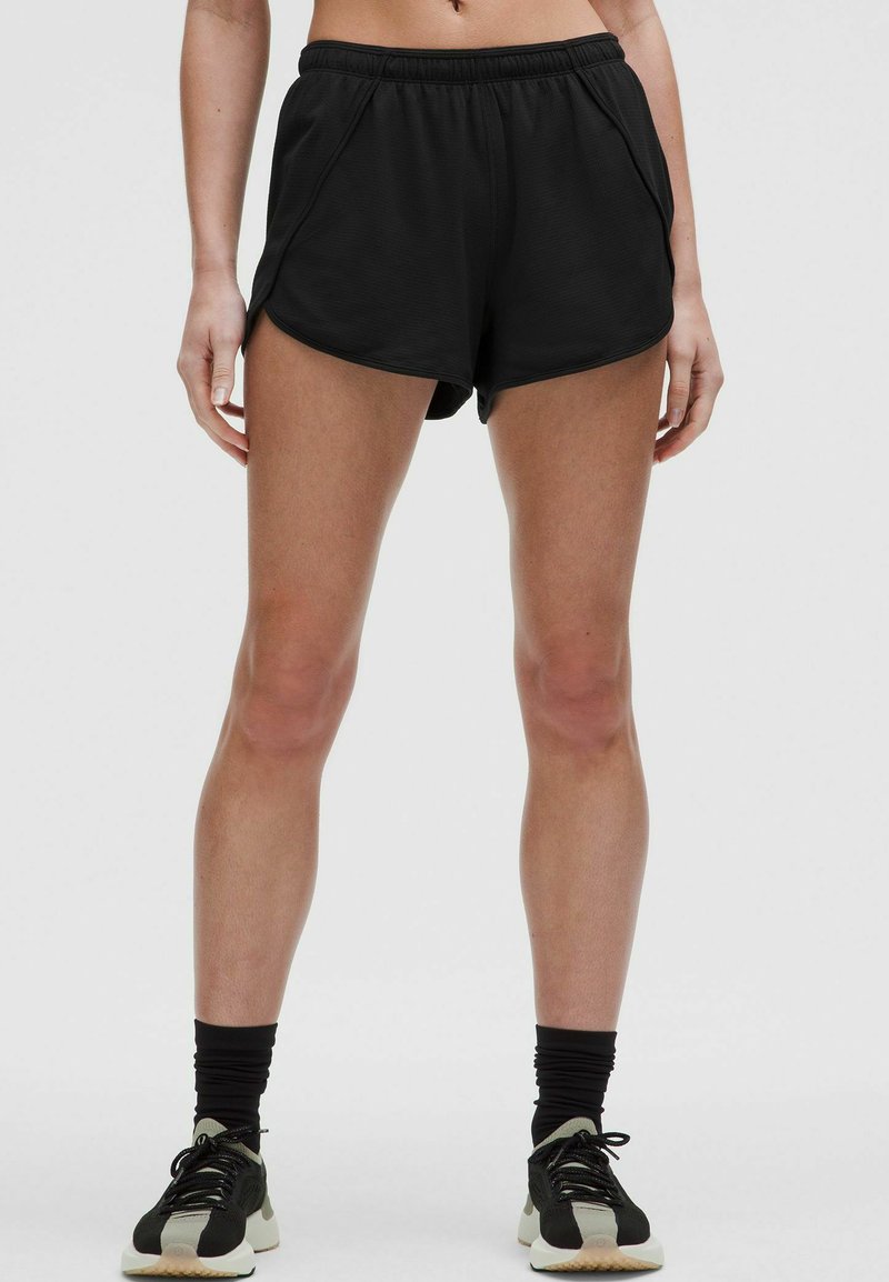 Pantalones cortos deportivos negros con un ajuste holgado y cintura elástica. Cuentan con bolsillos laterales y una textura suave, combinados con zapatos deportivos negros.