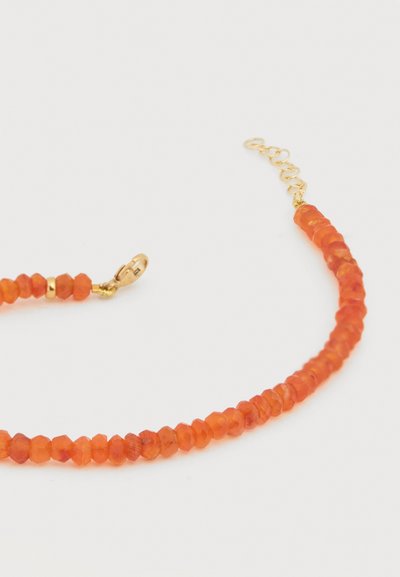 Πορτοκαλί στρογγυλό βραχιόλι με πολύεδρα, κούμπωμα από χρυσό και ρυθμιζόμενη αλυσίδα σε λευκό φόντο.