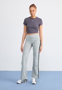 Grijze fitted broek met zwarte zijstrepen, gecombineerd met een grijze cropped T-shirt met een klein wit logo, aangevuld met zilveren sportschoenen.