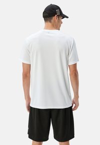 Maglietta sportiva bianca a maniche corte con una texture liscia, abbinata a pantaloni corti neri. Presenta un design minimal e un accento sottile a livello del collo.