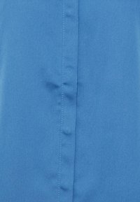 Blått tyg i närbild med en jämn textur. Har vertikala sömmar och lätt rynkor, vilket indikerar ett lätt material.