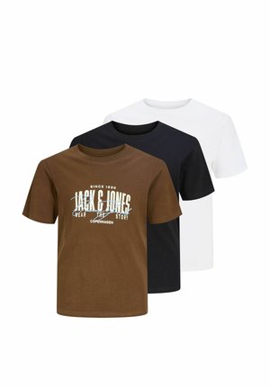Dreng med krøllet hår iført hvid grafisk t-shirt, falmede vidbenede jeans og beige sko, stående mod ensfarvet baggrund.