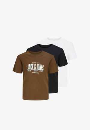 Dreng med krøllet hår iført hvid grafisk t-shirt, falmede vidbenede jeans og beige sko, stående mod ensfarvet baggrund.