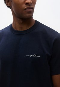 Tengerészkék pamut póló kerek nyakkivágással és rövid ujjakkal, bal mellrészen kis fehér hímzett logóval.