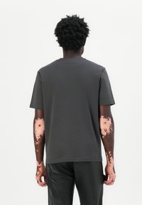 T-shirt noir court à manches courtes avec un col rond, fabriqué en tissu doux, vu de dos, associé à un pantalon noir.