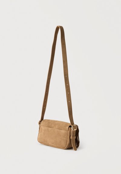 Μικρό ταμπά σακουλάκι ώμου από σουέτ με ρυθμιζόμενο λουρί και αγκράφα χρυσού τόνου σε απλό ανοιχτό φόντο.