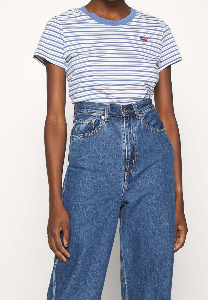 Personne portant un t-shirt rayé bleu et blanc Levi's rentré dans un jean en denim bleu taille haute avec passants de ceinture et poches avant.