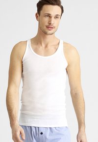 Débardeur en coton blanc avec un design sans manches, un col rond et une coupe ajustée. Style minimaliste, texture douce et apparence légère.