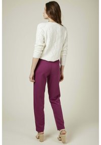 Pull en maille blanche à col roulé avec des manches longues, associé à un pantalon violet à coupe relaxée et des sandales à talons clairs. Fond uni.