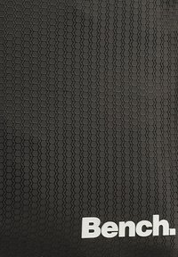 Schwarze, strukturierte Oberfläche mit hexagonalem Muster, das am unteren Rand ein weißes "Bench."-Logo zeigt. Das Design ist schlank und modern.
