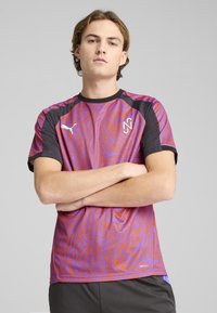 Camisa deportiva de patrón púrpura y rojo con mangas negras, que presenta un cuello redondo y detalles de marca. Ligera, con un ajuste atlético diseñado para el rendimiento.