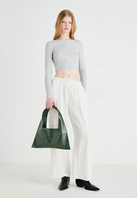 Green leather tote bag with a square handle, textured surface, and triangular shape, paired with a gray cropped top and white wide-leg pants.