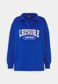 Blå sweatshirt med lång ärm och krage, med "LEISURE 1998" i krämfärgad brodering över bröstet. Mjuk textur.