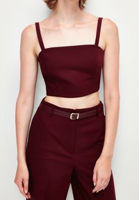 Burgundy kort topp med tunna remmar, tillverkad av slätt tyg. Matchas med matchande högmidjade byxor med bälte och spänne.