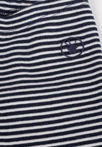 Tessuto a righe navy e bianche con una consistenza morbida. Include un piccolo logo ricamato in un design circolare sul lato sinistro superiore.