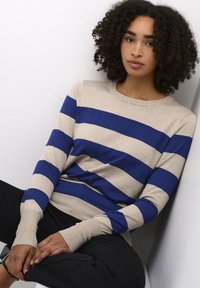 Knit sweater in beige with wide blue stripes, featuring a round neckline and long sleeves, displayed with a relaxed fit against a plain backdrop.