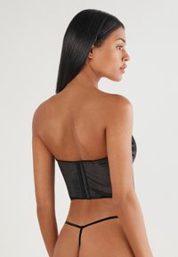Top de corsé negro sin tirantes con un diseño ajustado, textura suave y cierre de cremallera en la parte trasera. Combinado con un tanga negro minimalista.