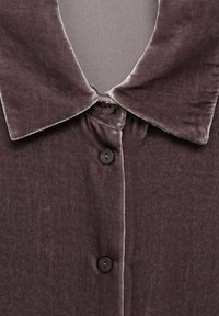 Camisa de terciopelo marrón con un cuello suave, bordes redondeados y dos botones en la parte delantera. La textura parece suave y ligeramente brillante.