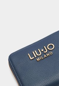 Tumši zila ādas maku ar teksturētu apdari, kuram ir zelta tonī izspiestā emblēma "LIU·JO MILANO" un rāvējslēdzēja aizsargmehānisms gar malu.