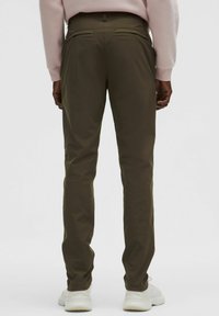 Olivově zelené kalhoty s přímým střihem, bočními kapsami a dvěma zadními kapsami. Nošeny s bílými teniskami a světle růžovou mikinou.