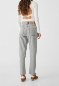 Jeans grises de talle alto con un corte relajado, que cuentan con dos bolsillos traseros, combinados con una blusa de manga larga acanalada con un diseño de espalda descubierta.