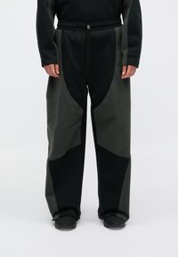 Pantalones de forro polar oscuros con paneles texturizados en diferentes tonalidades de negro y verde. Cuentan con una cintura con cordón y un ajuste holgado.