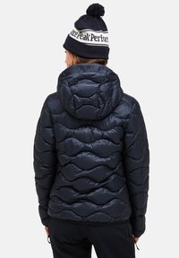 Navy puffer jacket with a quilted wave pattern, featuring a hood. The model wears a knitted hat with a pom-pom and logo.