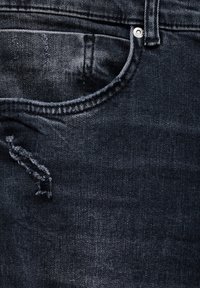 Jean en denim foncé avec une zone usée près de la poche, un bouton en métal argenté et un design classique à cinq poches. Texture lisse.