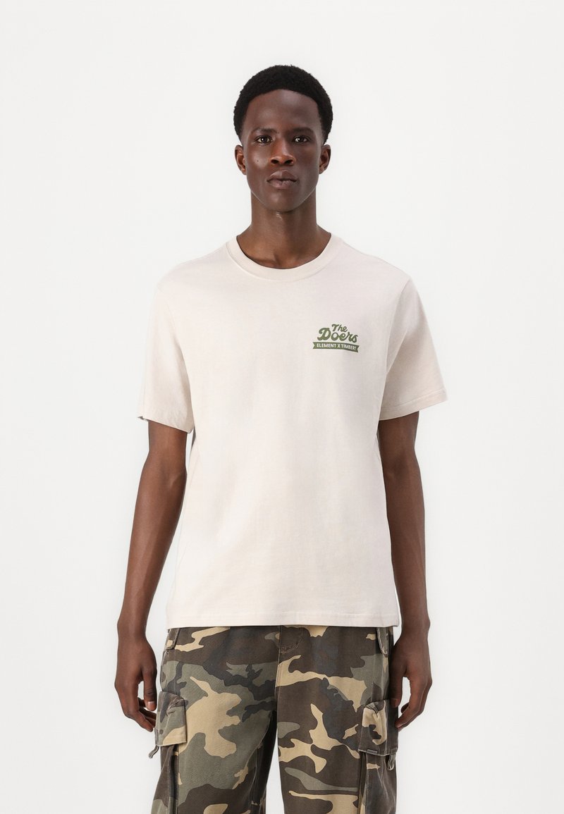 Cremefarvet bomulds T-shirt med korte ærmer, rund halsudskæring og grønt grafisk logo på brystet. Bæres med camouflage cargo bukser.